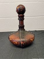 Front and slightly angled left view of vintage Italian leather decanter showing bulbous body, rivet detailing and stopper.