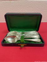 Six silver plated spoons arranged in their fitted dark case with green silk interior showing the handle pattern and spoon shape.