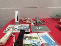 Full view of the Wii console, two game controllers, sensor bar, gaming cables, instruction manuals, and three game cases including Wii Sports, Wii Sports Resort, and Mario Kart Wii.