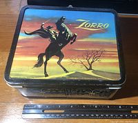 Top view showing painted metal lid with Zorro on horse image and ruler indicating size.