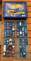 Top-down view of the blue Hot Wheels carrying case with flame graphics and over 40 blue die-cast cars arranged inside trays.