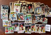 Lot of hockey cards spread out showing various players, stat leader cards, and team cards mostly from 1976-77 and 1977-78 with visible warping and damage.