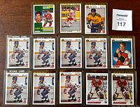 Top-down photo of 13 rookie cards spaced out on a wood surface. Cards are in clear protective holders showing player images and rookie card markings.