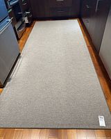 Full view of the rectangular gray area rug laid on a kitchen floor with dark cabinetry around it.