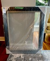 Full front view of wooden frame wrapped in plastic, dark stained wood with grooved edges.