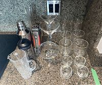 Overall view of the barware and glassware set on countertop including shaker, glasses, mixing glass, martini glasses, and bar tool.