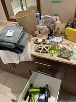 Photo of bathroom counter displaying folded towels, assorted bath and tooth care items, and toiletry bottles.