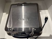 Closed stainless steel waffle maker with Cuisinart logo on top and power cord visible