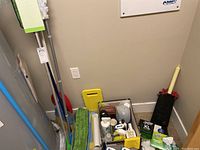 Photo of Swiffer style floor mops and various cleaning supplies organized on the floor including cleaning cloths, bottles, gloves, and sponges.