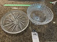 Two crystal glass serving pieces side by side on a kitchen countertop—a round plate with starburst pattern and a footed bowl with diamond cut design.
