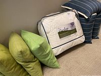 Photo showing the packaged white goose down duvet labeled 'Prestige' along with several cushions in different shades of green.