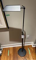 Full view of the floor lamp showing its black base, stand, and silver rectangular shade attached to an adjustable arm.