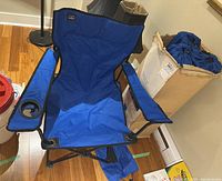 Blue folding camp chair with padded armrests and cup holder, open and set up for use, showing seat and back.