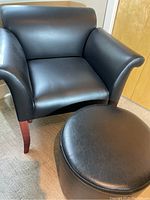 Full view of black synthetic leather armchair with matching round ottoman on wooden legs