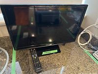 Samsung 24-inch TV placed on a countertop with remote control in front of it.