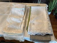 Assorted folded linens on a table showing stacked linen pieces with lace edges and embroidery detail