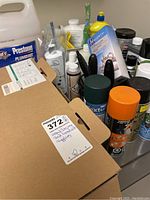 Overall view of assorted household cleaners, spray paint cans, and a cardboard box with Holife vacuum cleaner label