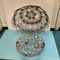 Smaller wire bowl with multiple circular shells installed within its spiral wire design shown from a front angle.
