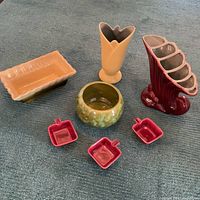 Seven collectible pottery pieces arranged on floor showing various planter, vase, and ashtray shapes and colors