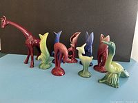 Photo showing the full 9-piece set including 5 cornucopia bud vases, 2 decorative deer, 1 red giraffe, and 1 green bird against black backdrop.