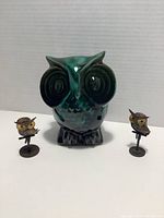 Front view of the green glazed ceramic owl bank with two small metal owl figurines on each side showing size comparison and condition.