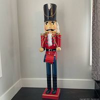 Front view of the 4 ft tall wooden Christmas nutcracker, showing red, blue, black, and gold painted uniform with feather on hat.