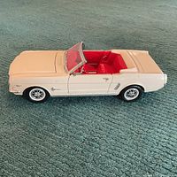 Side profile of white 1/18 scale Ford Mustang diecast model showing closed hood, trunk, and doors with red interior.