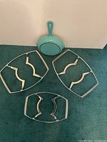 Blue Le Creuset pan with handle and six silver-tone CorningWare metal serving stands on a carpeted floor