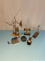 Photo showing all six items: two metal art statues, Lucite paperweight with curling stones, Florida Lucite souvenir, curling liquor bottle, and decorative bell.