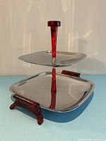 Two-tier chrome serving tray viewed from side angle showing red Bakelite handle and feet.