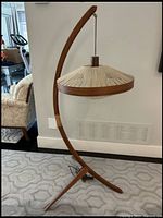 Front view of teak curved tripod floor lamp with woven shade