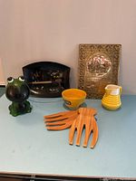 Photo of the full lot showing the frog bank, black San Francisco souvenir tray, yellow ceramic bowl, wooden salad serving utensils, brass Bless This House plaque, and yellow ceramic pitcher.