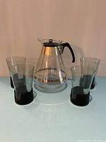 Full view of Pyrex 12 cup coffee carafe surrounded by four Corning Snap glasses with black removable bases and smokey inserts