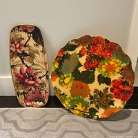 Both 1960s vintage Lucite serving trays displayed side by side against a white wall, showing size and floral pattern difference.