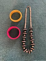 Photo showing a vintage black and beige beaded necklace laid flat with two Lucite bangles, one yellow and one pink, on a fabric surface.