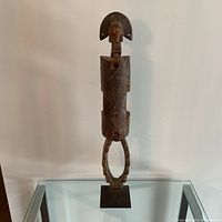 Front view of the wooden Dogon tribal lock mounted on metal stand, showing elongated human figure with geometric headpiece.