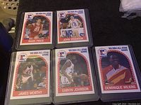 Five 1989 NBA All-Star basketball cards including Mark Price, John Stockton, James Worthy, Earvin Johnson, and Dominique Wilkins shown in protective sleeves.