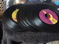Stack of 21 black vinyl 45 RPM records with mixed colorful center labels visible on top and side of the pile.