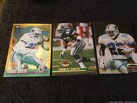 Three Emmitt Smith football collectible cards laid flat on a dark cloth, showing varying action poses and uniform details.