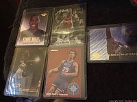 Five basketball player cards laid out on a dark cloth, including portraits and action shots, all in protective plastic sleeves.