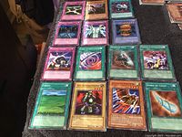 20 Yu-Gi-Oh! Konami collectible cards laid out in a grid on a carpeted surface, featuring monsters, spells, and trap cards in sleeves.