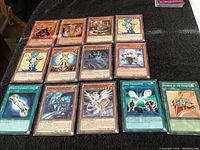 Top view of 15 Yu-Gi-Oh! cards laid out on a dark surface showing various characters and spell effects.