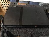 Photo of black Sony PlayStation 2 slim console showing top and front, placed on dark towel