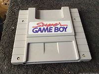 Front side of the Super Game Boy cartridge showing the colorful Super GAME BOY label on gray plastic cartridge.