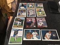 Top view of thirteen vintage baseball cards laid out on black cloth. Cards feature various baseball players in different poses including pitching, batting and illustrated portraits. Colors and designs appear typical of vintage Upper Deck and Topps cards.