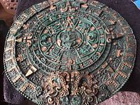 Full photo of the circular carved stone plaque with intricate Aztec calendar design, showing overall shape, paint, and repair.