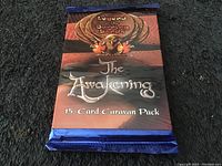 Front of the unopened 15-card caravan pack showing the 'Legend of the Burning Sand - The Awakening' design and colorful blue foil wrapping.