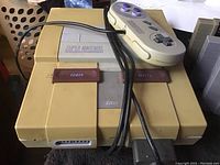 Super Nintendo Entertainment System console with power and reset buttons visible, controller resting on top with its cable wrapped over console