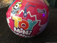 Spherical pink capsule showing Zuru Series 2 Toy Mini Brands collectible logo and branding with text 'Collect all 100 toys'.