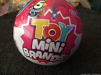 Front view of spherical packaging showing the 'Toy Mini Brands' logo and '5 Surprise' text in bright colors